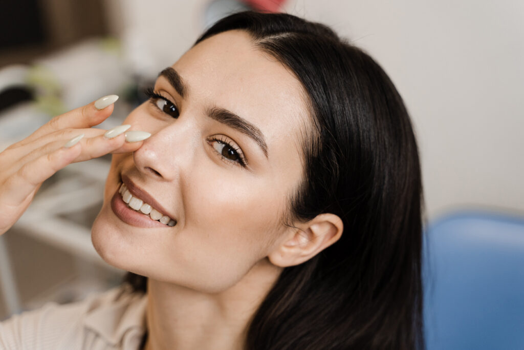 Woman smiling and touching her nose after rhinoplasty in Pittsburgh, PA