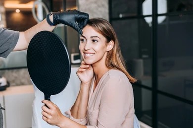 Woman looking in the mirror at her lifted brows from a brow lift in Pittsburgh, PA