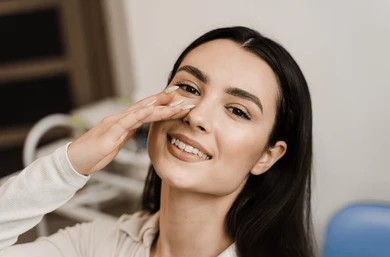 Woman smiling and touching her nose after rhinoplasty in Pittsburgh, PA